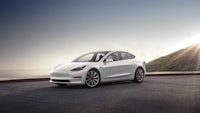 the white tesla model 3 is parked in front of a mountain